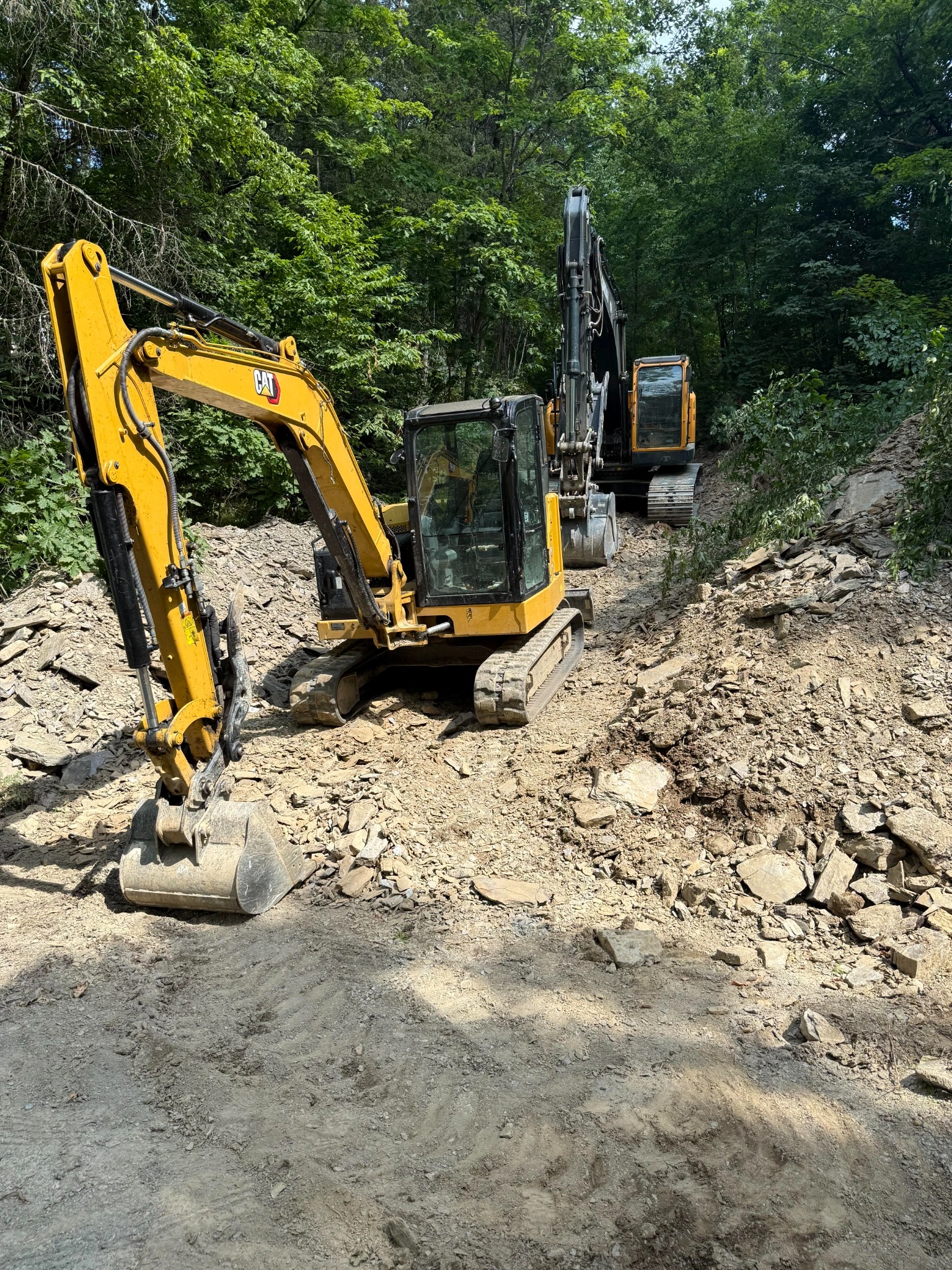 Yellow construction equipment creating access path through wooded area