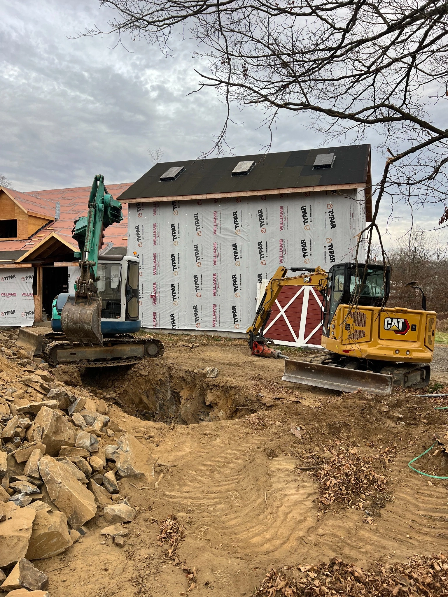 Excavators digging foundation near barn under construction