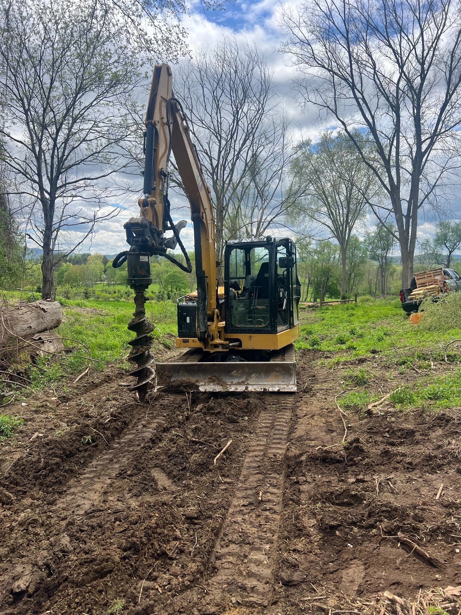 Excavator digging utility trenches toward new building under construction