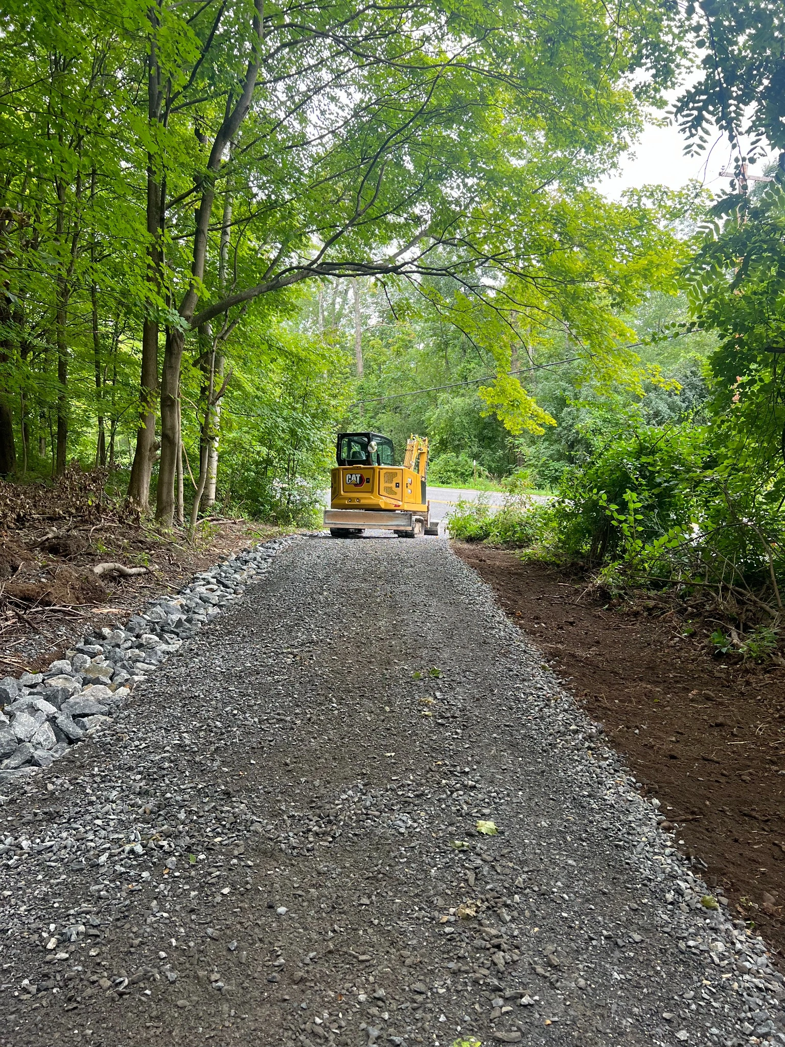 Excavator compacting gravel driveway leading to roadway